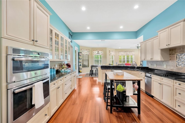 kitchen featuring stainless steel appliances, dark stone counters, tasteful backsplash, light hardwood / wood-style flooring, and sink