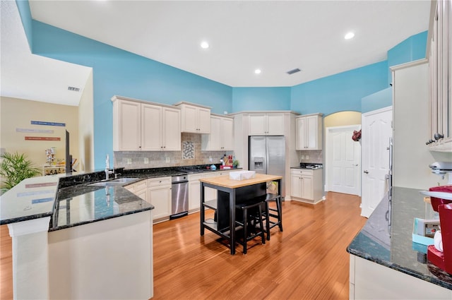 kitchen with dark stone counters, white cabinets, light wood-type flooring, backsplash, and sink