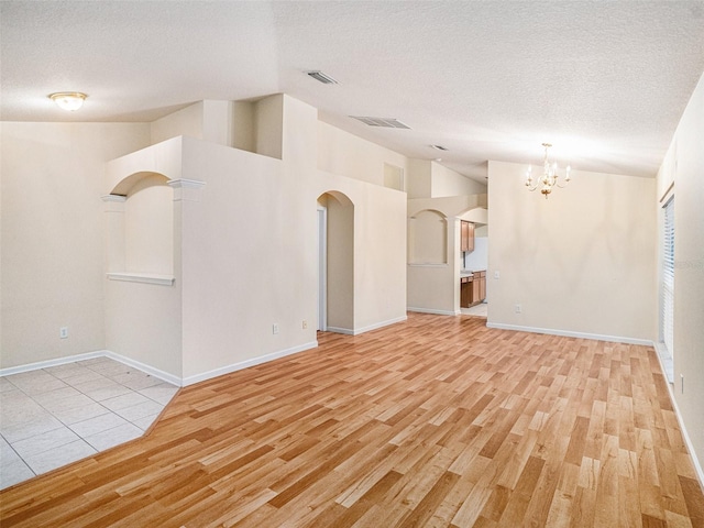 spare room featuring a textured ceiling, vaulted ceiling, a chandelier, and light hardwood / wood-style floors