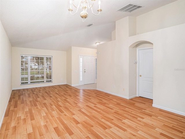 unfurnished living room with light wood-style floors, visible vents, arched walkways, and a chandelier