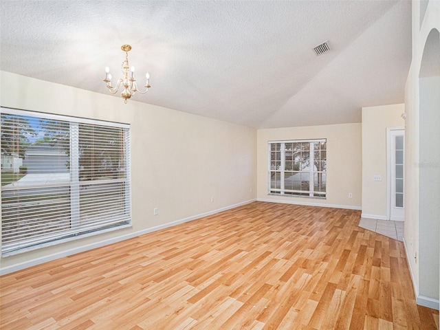 spare room featuring a textured ceiling, light wood-style flooring, visible vents, vaulted ceiling, and an inviting chandelier