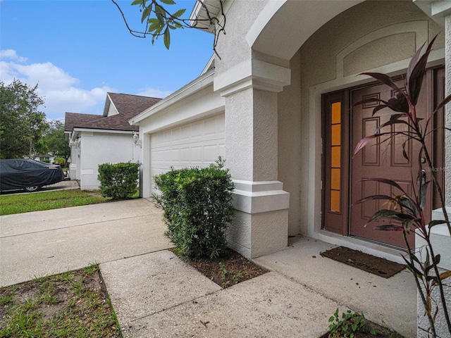 property entrance with an attached garage, driveway, and stucco siding