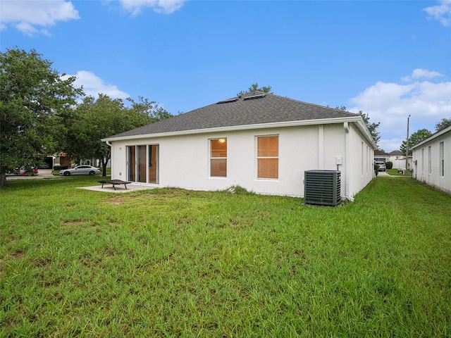 back of property featuring central air condition unit, roof with shingles, a lawn, and stucco siding