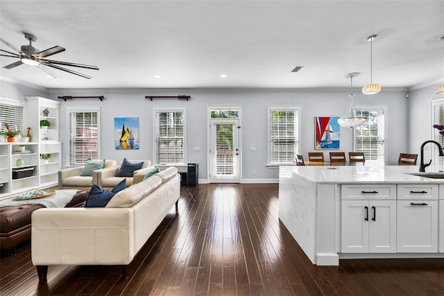 living room featuring ceiling fan with notable chandelier, ornamental molding, sink, and dark wood-type flooring