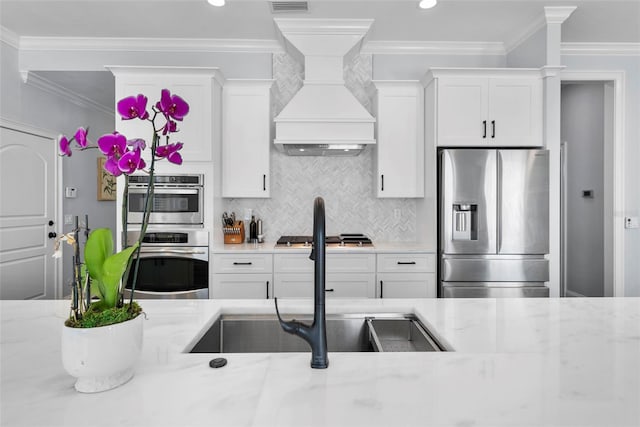 kitchen featuring appliances with stainless steel finishes, light stone counters, ornamental molding, sink, and white cabinets