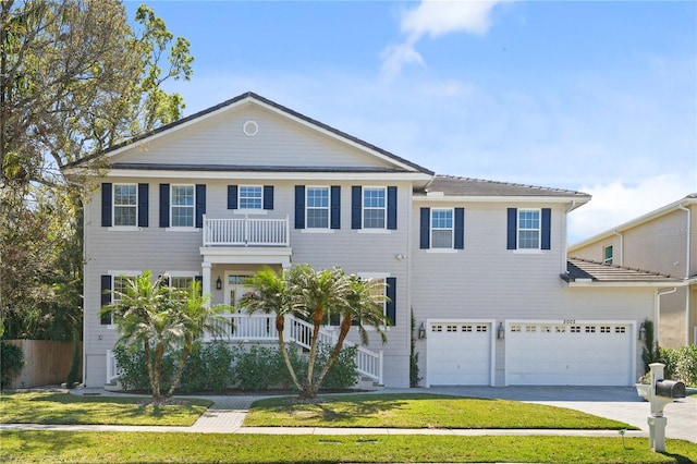 view of front of property featuring a front lawn, a balcony, an attached garage, and driveway