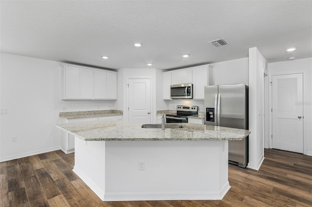 kitchen with stainless steel appliances, white cabinets, a center island with sink, light stone counters, and dark hardwood / wood-style flooring