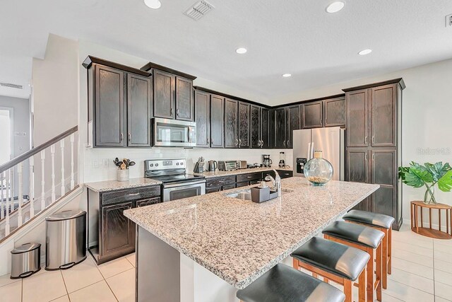 kitchen featuring an island with sink, light stone countertops, sink, and stainless steel appliances