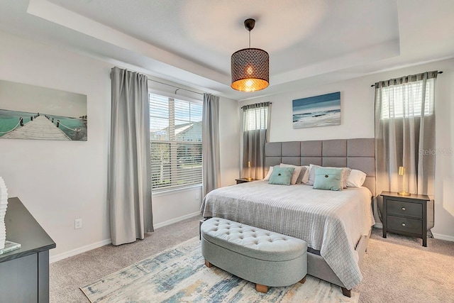 bedroom with a raised ceiling, light colored carpet, and multiple windows