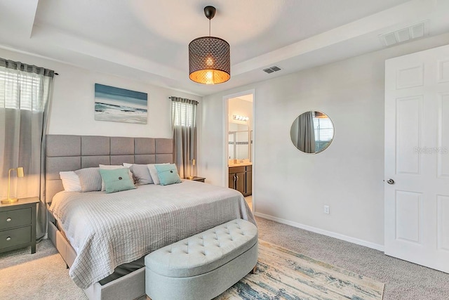 bedroom featuring connected bathroom, light colored carpet, and a tray ceiling