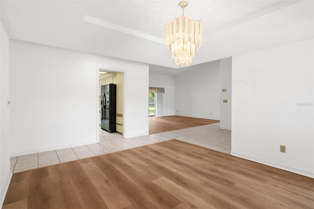 empty room featuring an inviting chandelier, light hardwood / wood-style floors, and a textured ceiling