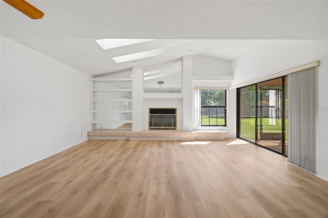 unfurnished living room featuring built in shelves, light hardwood / wood-style floors, a tile fireplace, and a textured ceiling