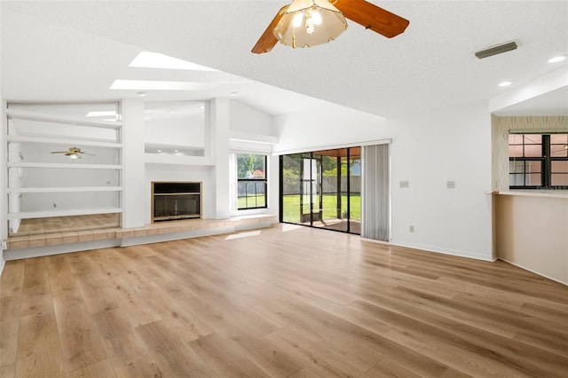 unfurnished living room featuring lofted ceiling with skylight, ceiling fan, a fireplace, a textured ceiling, and light hardwood / wood-style floors