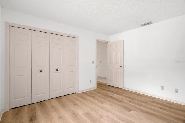 unfurnished bedroom featuring a closet, a textured ceiling, and light wood-type flooring