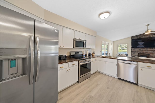 kitchen with a brick fireplace, appliances with stainless steel finishes, lofted ceiling, white cabinets, and light wood-type flooring