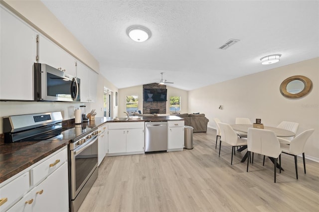 kitchen with appliances with stainless steel finishes, vaulted ceiling, light wood-type flooring, and white cabinetry