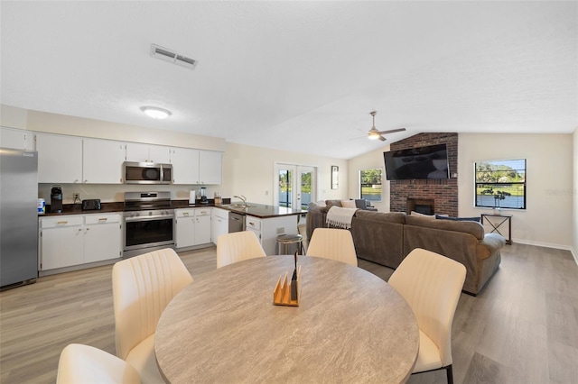 dining room featuring plenty of natural light, light hardwood / wood-style floors, vaulted ceiling, and a fireplace