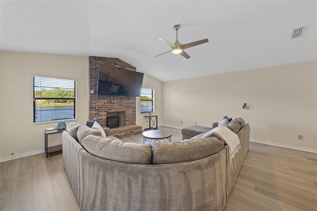 living room featuring ceiling fan, a brick fireplace, light hardwood / wood-style floors, lofted ceiling, and brick wall