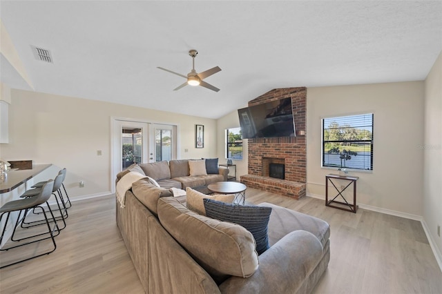 living room with a healthy amount of sunlight, light wood-type flooring, a brick fireplace, and lofted ceiling