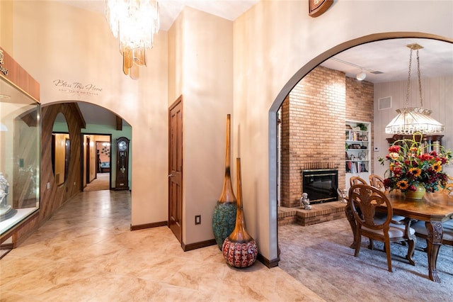 interior space featuring a chandelier, rail lighting, a fireplace, light tile flooring, and a high ceiling