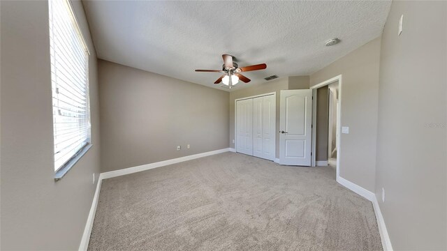 unfurnished bedroom featuring ceiling fan, a textured ceiling, light colored carpet, and a closet