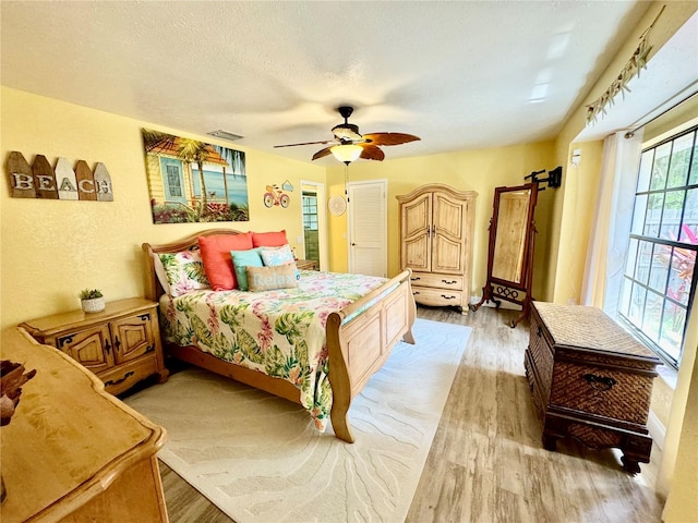 bedroom featuring a textured ceiling, ceiling fan, multiple windows, and light hardwood / wood-style flooring