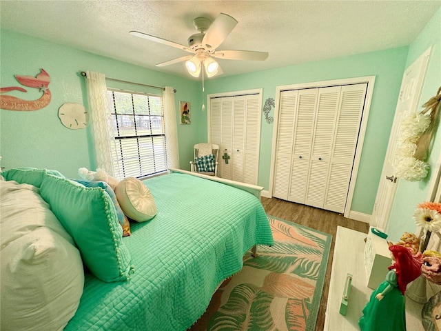 bedroom featuring a textured ceiling, ceiling fan, wood-type flooring, and two closets