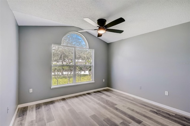 empty room with a textured ceiling, ceiling fan, vaulted ceiling, and light wood-type flooring