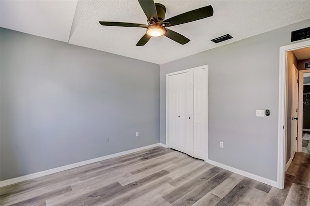 unfurnished bedroom with ceiling fan, a closet, light hardwood / wood-style floors, and a textured ceiling