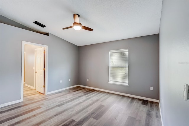 empty room with lofted ceiling, a textured ceiling, ceiling fan, and light wood-type flooring