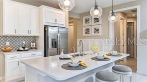 kitchen featuring a breakfast bar, a center island with sink, white cabinetry, stainless steel fridge, and backsplash