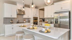 kitchen featuring hanging light fixtures, tasteful backsplash, a kitchen island with sink, wall chimney exhaust hood, and white cabinets