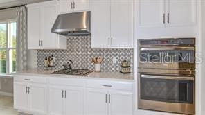 kitchen featuring backsplash, white cabinetry, plenty of natural light, and wall chimney exhaust hood