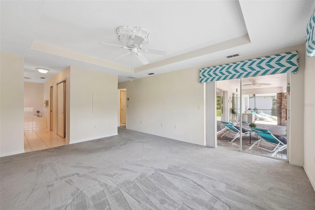 unfurnished room with a raised ceiling, ceiling fan, and light colored carpet