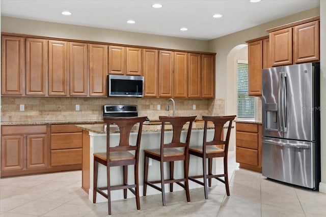 kitchen with light stone countertops, tasteful backsplash, a kitchen bar, a kitchen island, and appliances with stainless steel finishes