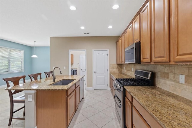 kitchen with stainless steel appliances, hanging light fixtures, light stone countertops, a breakfast bar, and sink