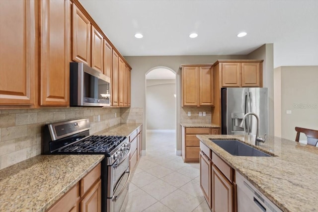 kitchen with appliances with stainless steel finishes, light tile patterned floors, light stone counters, sink, and tasteful backsplash