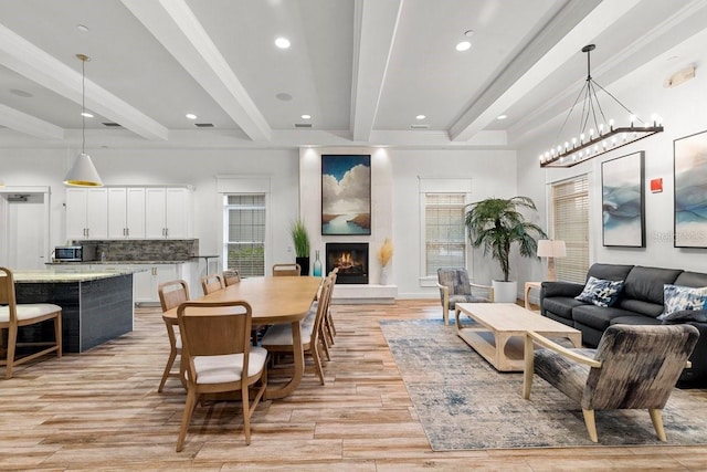 dining room with a fireplace, a notable chandelier, light hardwood / wood-style floors, and beamed ceiling