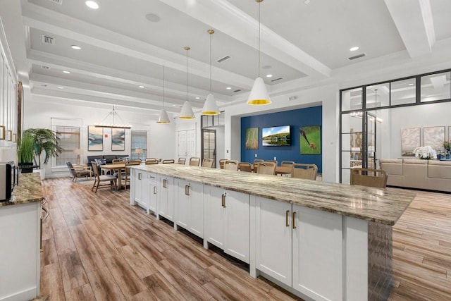 kitchen with a breakfast bar area, hanging light fixtures, light stone countertops, beam ceiling, and white cabinets