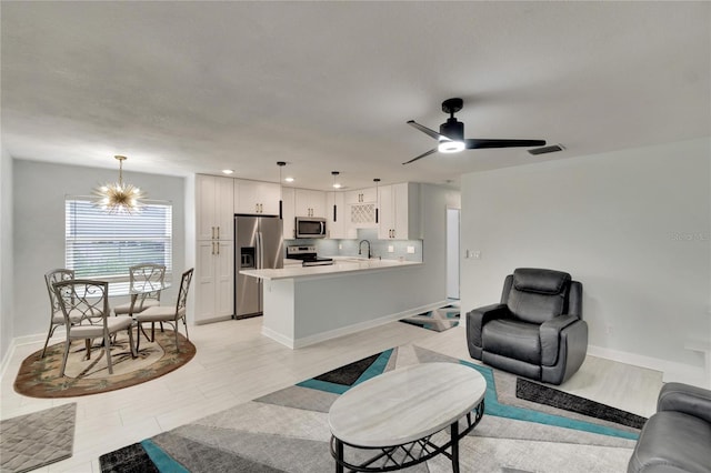 living room featuring ceiling fan with notable chandelier and sink