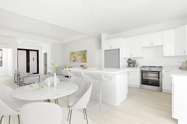 kitchen featuring white cabinetry, light wood-type flooring, stainless steel gas range oven, and a kitchen breakfast bar