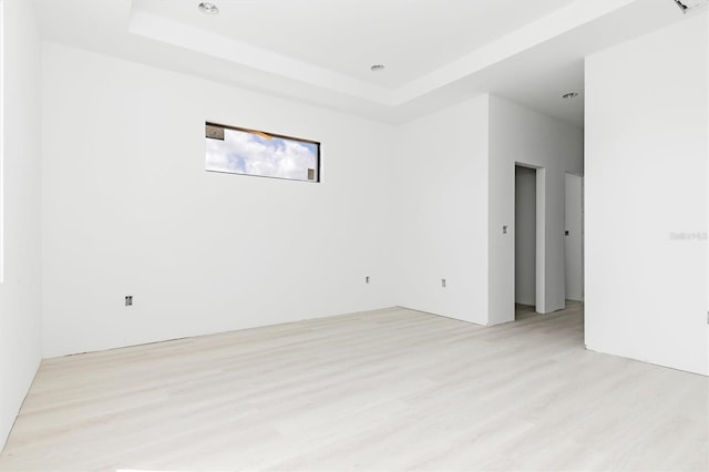 empty room featuring a raised ceiling and light hardwood / wood-style flooring