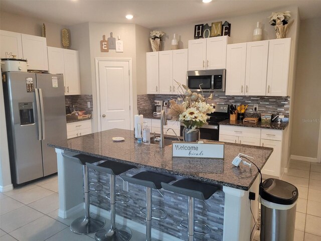 kitchen with white cabinets, a center island with sink, backsplash, and stainless steel appliances