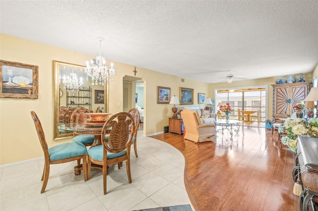 tiled dining room featuring ceiling fan with notable chandelier and a textured ceiling