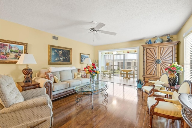 living room featuring ceiling fan, dark wood-type flooring, and a textured ceiling