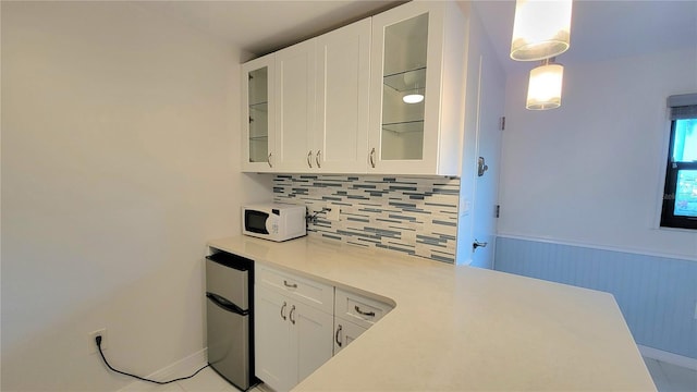 kitchen featuring pendant lighting, decorative backsplash, white cabinetry, and stainless steel refrigerator