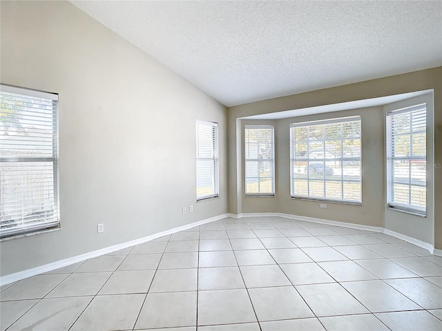unfurnished room with light tile patterned floors, a wealth of natural light, vaulted ceiling, and a textured ceiling