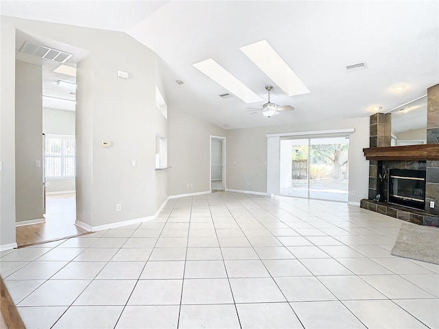 unfurnished living room with high vaulted ceiling, a skylight, a tiled fireplace, light tile patterned floors, and ceiling fan