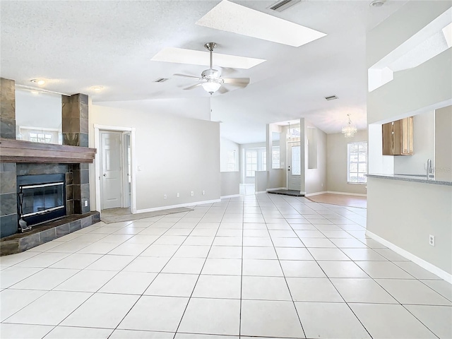 unfurnished living room with lofted ceiling with skylight, ceiling fan with notable chandelier, a tile fireplace, and light tile patterned floors