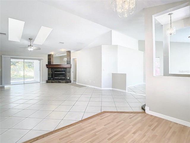 unfurnished living room with light tile patterned floors, ceiling fan with notable chandelier, and a tile fireplace
